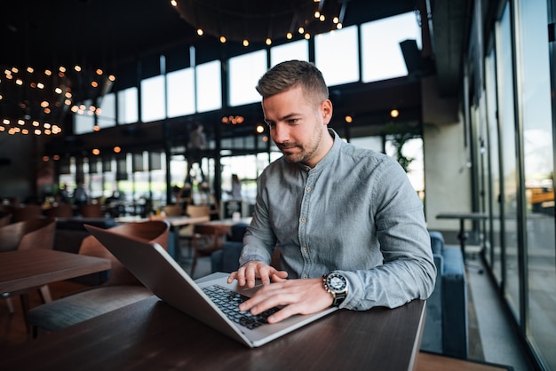 Młody przystojny freelancer pracuje na laptopie w nowożytnej kawiarni.