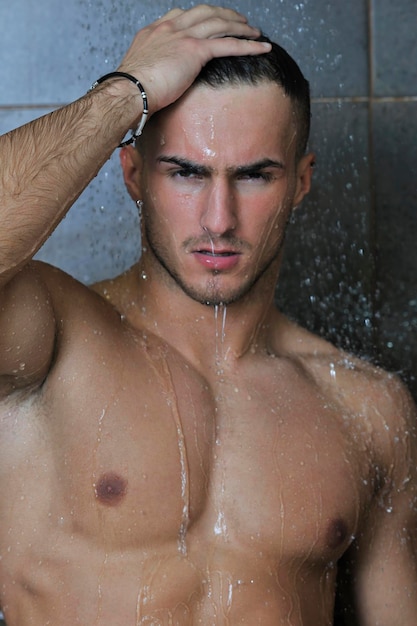 młody przystojny i atrakcyjny mężczyzna z mokrym muskularnym ciałem biorący showe w kąpieli z czarnymi kafelkami w tle