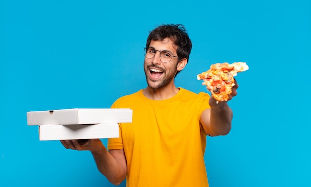 Młody przystojny indyjski mężczyzna ze szczęśliwym wyrazem twarzy i trzymający pizze na wynos
