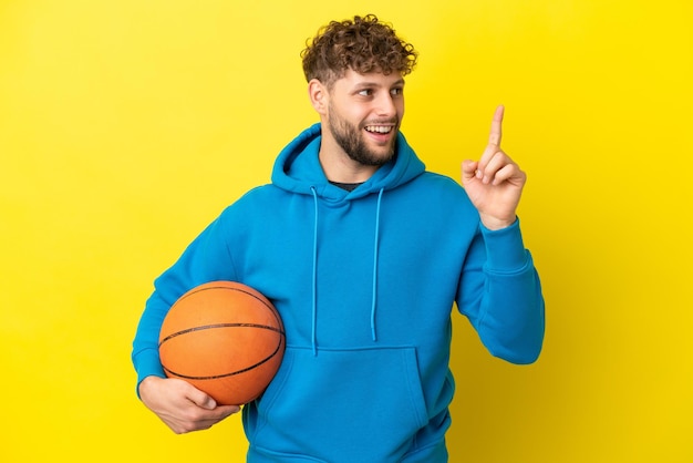 Młody przystojny kaukaski mężczyzna na żółtym tle gra w koszykówkę i ma pomysł