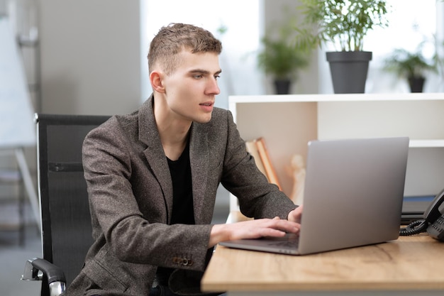 Młody przystojny menedżer pracujący w biurze na laptopie