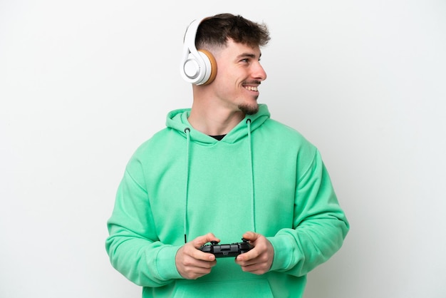 Młody przystojny mężczyzna bawiący się kontrolerem gier wideo na białym tle patrząc z boku