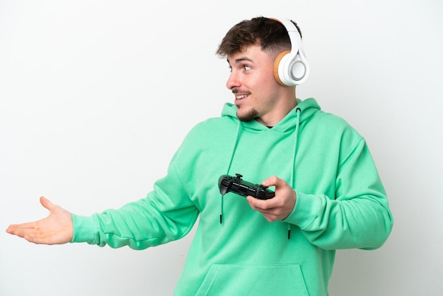 Młody przystojny mężczyzna bawiący się kontrolerem gier wideo na białym tle z wyrazem zaskoczenia, patrząc z boku