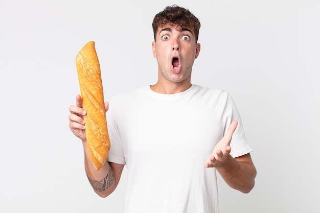 młody przystojny mężczyzna czuje się bardzo zszokowany i zaskoczony i trzyma bagietkę z chlebem