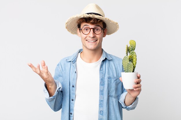 Młody przystojny mężczyzna czuje się szczęśliwy, zaskoczony, realizując rozwiązanie lub pomysł. rolnik trzymający ozdobnego kaktusa