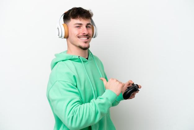 Młody przystojny mężczyzna grający z kontrolerem gier wideo na białym tle dumny i samozadowolony