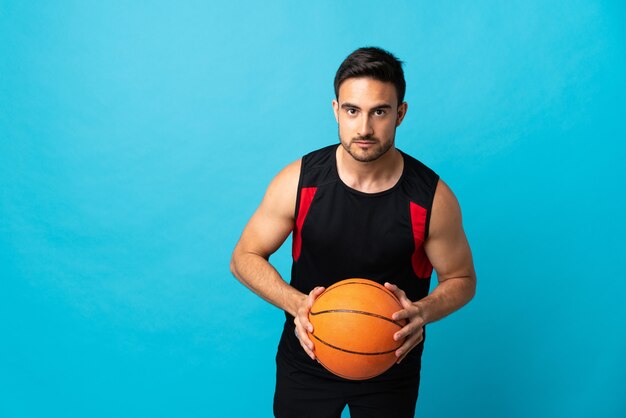 Zdjęcie młody przystojny mężczyzna na białym tle na niebieskim tle gry w koszykówkę