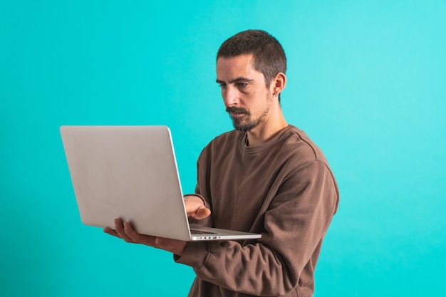 Młody przystojny mężczyzna na białym tle na niebieskim tle przy użyciu swojego laptopa