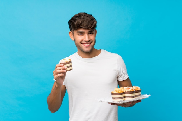 Młody przystojny mężczyzna nad odosobnioną błękit ścianą trzyma mini torty