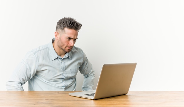 Młody przystojny mężczyzna pracuje z jego laptopem ufny utrzymuje ręki na biodrach.