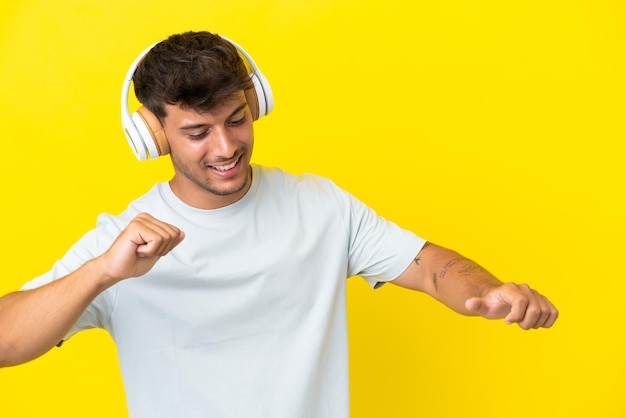 Młody przystojny mężczyzna rasy kaukaskiej odizolowany na żółtym tle słuchania muzyki i tańca