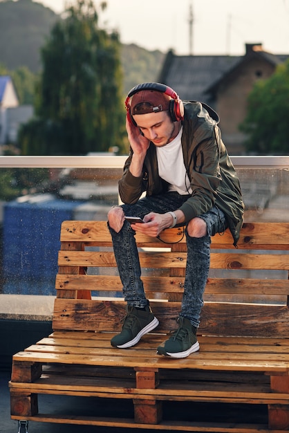 Młody przystojny mężczyzna słuchania muzyki w słuchawkach i przy użyciu telefonu na dachu budynku przemysłowego o zachodzie słońca.