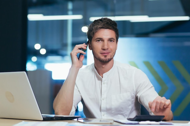 Młody przystojny mężczyzna specjalista pracujący w biurze przy biurku Rozmawia przez telefon komórkowy z klientami z bankiem z partnerami biznesowymi