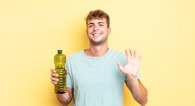 Młody przystojny mężczyzna uśmiecha się radośnie, machając ręką, witając cię i pozdrawiając. koncepcja oliwy z oliwek