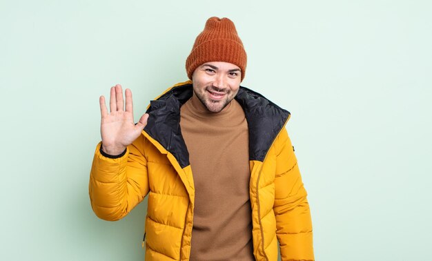 Młody Przystojny Mężczyzna Uśmiecha Się Radośnie Machając Ręką Witającą Cię I Witającą Cię W Zimnej Pogodzie