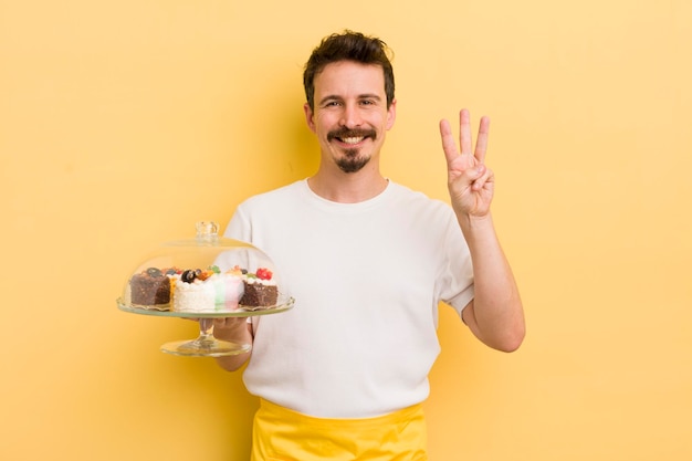 Młody przystojny mężczyzna uśmiechający się i patrzący przyjaźnie, pokazujący koncepcję ciastek domowej roboty numer trzy