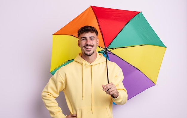 Młody przystojny mężczyzna uśmiechający się szczęśliwie z ręką na biodrze i pewny siebie. koncepcja parasola