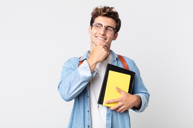 Młody Przystojny Mężczyzna Uśmiechający Się Ze Szczęśliwym, Pewnym Siebie Wyrazem Twarzy Z Ręką Na Brodzie. Koncepcja Studenta Uniwersytetu