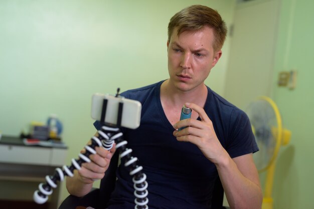Zdjęcie młody przystojny mężczyzna vlogging z inhalatorem astmy w domu