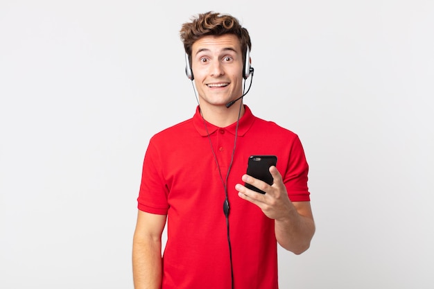 Młody przystojny mężczyzna wyglądający na szczęśliwego i mile zaskoczonego smartfonem i zestawem słuchawkowym