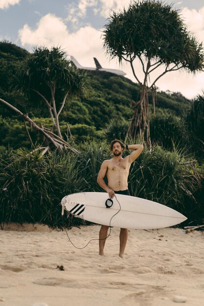 Młody przystojny mężczyzna z deską surfingową na oceanie.