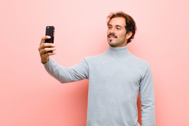 Młody przystojny mężczyzna z mądrze telefonem przeciw różowej płaskiej ścianie