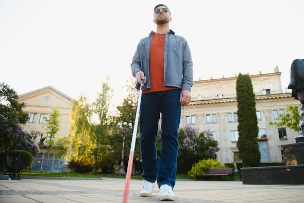 Młody przystojny niewidomy mężczyzna spacerujący z kijem po mieście