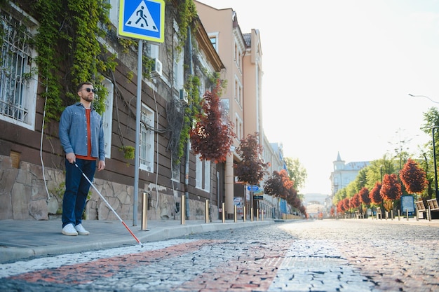 Młody przystojny niewidomy mężczyzna spacerujący z kijem po mieście