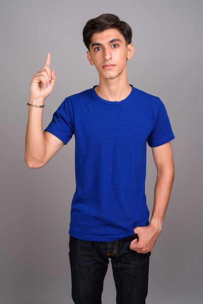 Młody przystojny Perski nastoletni chłopak wskazując palcem na szarym tle