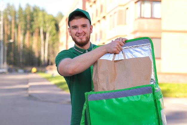 Zdjęcie młody przystojny szczęśliwy kurier uśmiechnięty mężczyzna dostarczający jedzenie z zielonym termosem