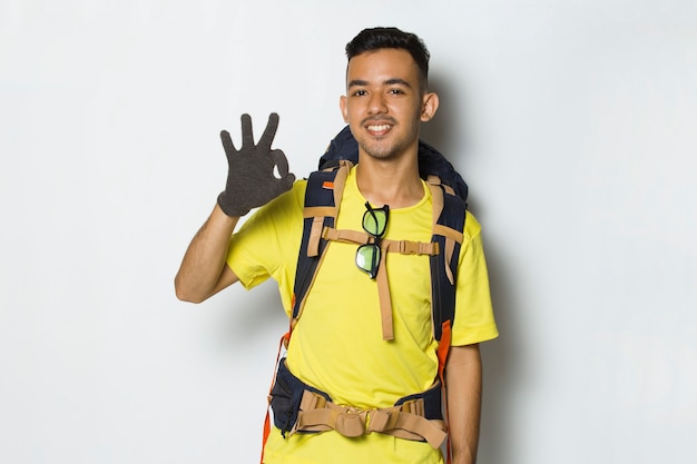 Młody przystojny turysta mężczyzna z plecakiem pokazując kciuk do góry ok gest na białym tle