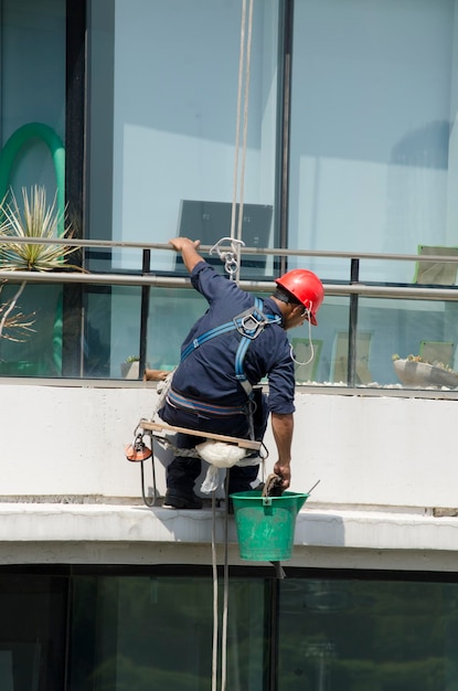 Młody robotnik czyści szkło szklanego budynku wiszącego z wysokości