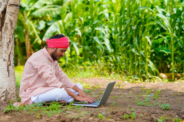 Młody rolnik indyjski za pomocą laptopa w dziedzinie rolnictwa.
