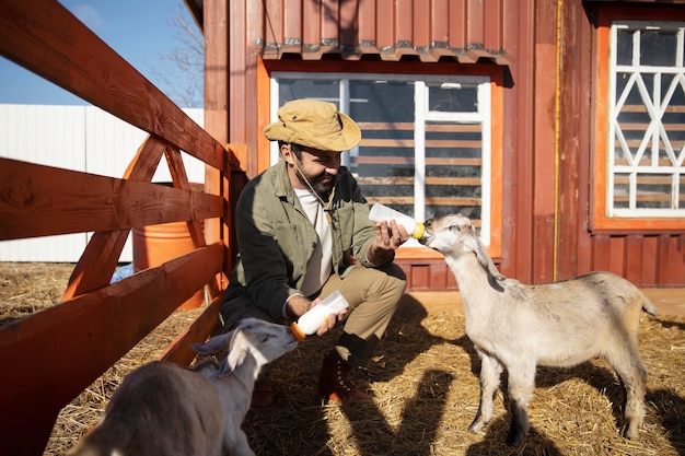 Zdjęcie młody rolnik karmiący swoje kozie mlekiem z butelki na farmie