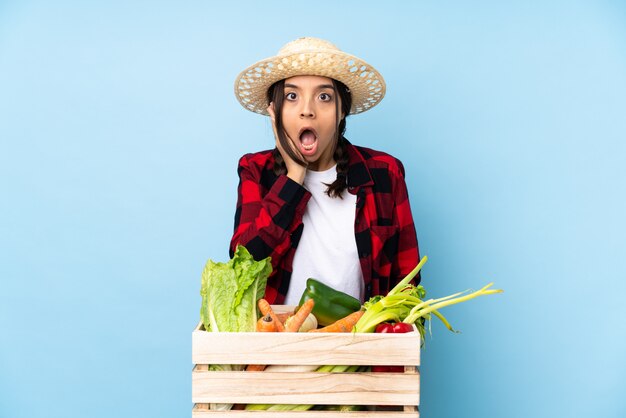 Młody rolnik Kobieta trzyma świeże warzywa w drewnianym koszu z niespodzianką i zszokowanym wyrazem twarzy