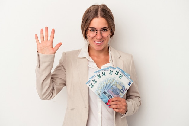 Młody rosyjski biznes kobieta trzyma banknoty na białym tle uśmiechnięty wesoły pokazywanie numer pięć palcami.