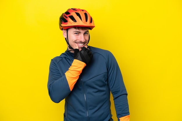 Młody rowerzysta kaukaski mężczyzna odizolowany na żółtym tle, patrząc w bok i uśmiechnięty