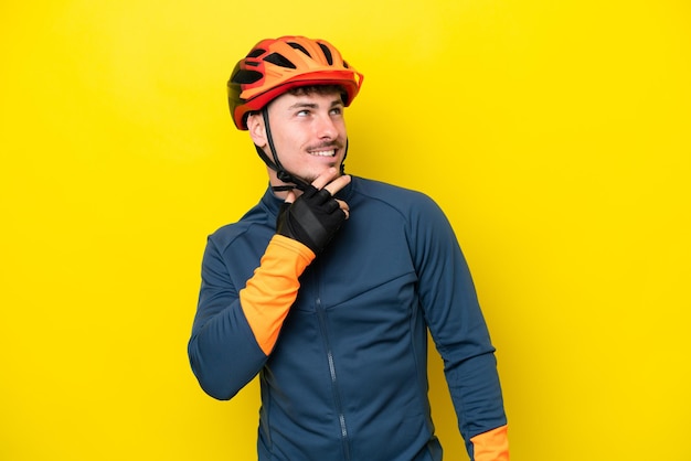 Młody rowerzysta kaukaski mężczyzna odizolowany na żółtym tle patrząc w górę podczas uśmiechania się