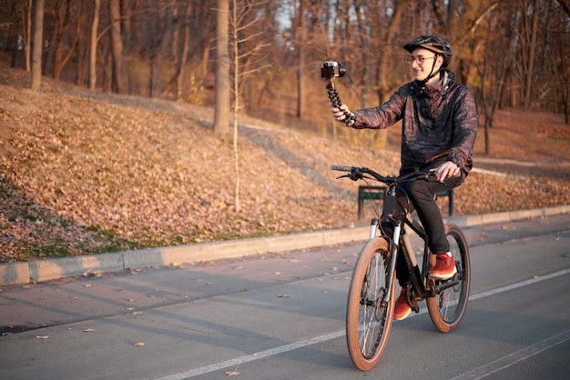 Zdjęcie młody rowerzysta vlogging w parku z bicyklem