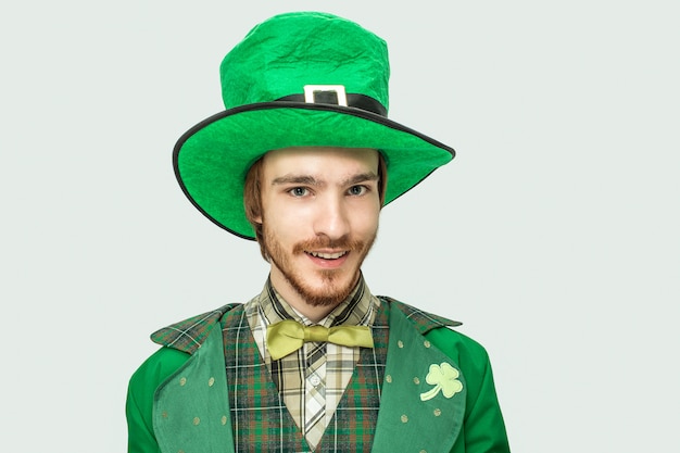 Zdjęcie młody rudy mężczyzna w zielonym kostiumie i kapeluszu świętego patryka wygląda prosto. pojedynczo na białym.