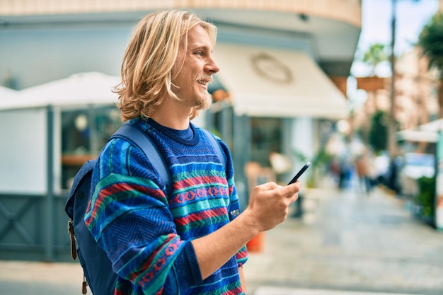 Młody skandynawski student uśmiechający się szczęśliwy za pomocą smartfona w mieście