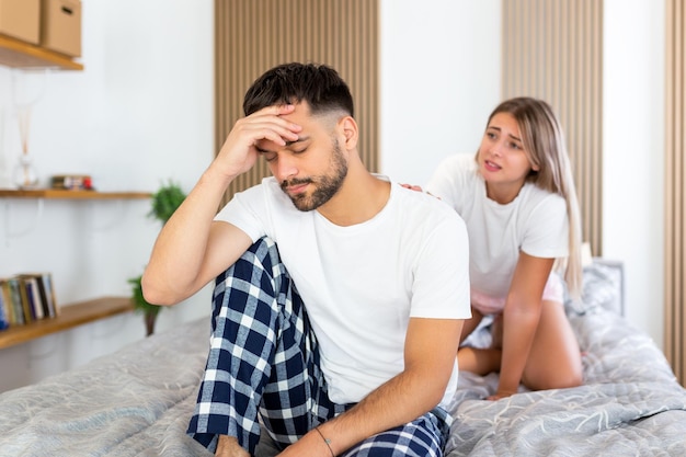 Młody smutny mężczyzna siedzi na łóżku po kłótni z żonami hotelowymi relacjami podróżniczymi i koncepcją problemów seksualnych zdenerwowany mężczyzna siedzący na łóżku z kobietą na plecach