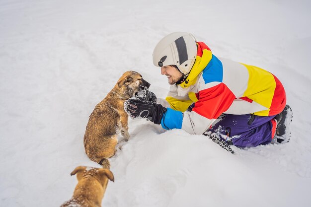 Młody snowboardzista bawi się ze szczeniakami w ośrodku narciarskim zimą
