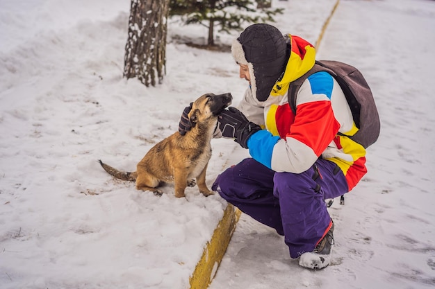 Młody snowboardzista bawi się ze szczeniakami w ośrodku narciarskim zimą