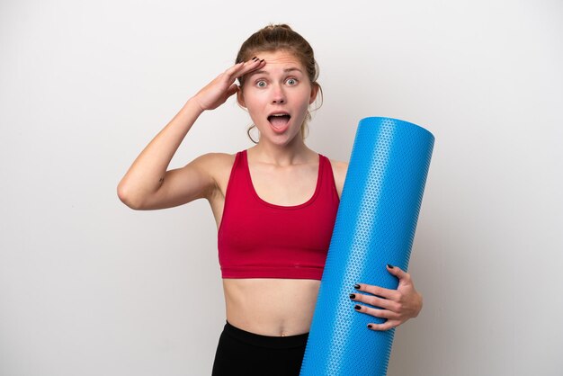 Młody sport Angielka idzie na zajęcia jogi, trzymając matę odizolowaną na białym tle z wyrazem zaskoczenia