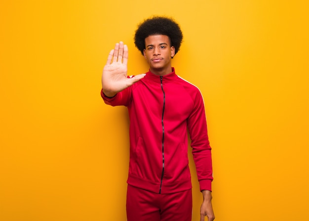 Młody sport czarny człowiek nad pomarańczową ścianą kładąc rękę z przodu