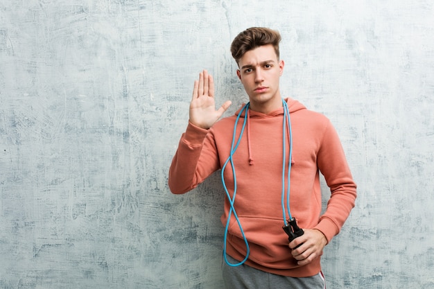 Młody Sport Człowiek Trzyma Skakankę Stojący Z Wyciągniętą Ręką Pokazując Znak Stop, Zapobiegając Ci.