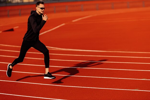 Młody Sportowiec Biega Po Stadionie Ubrany W Czarną Odzież Sportową, Przygotowując Się Do Zawodów