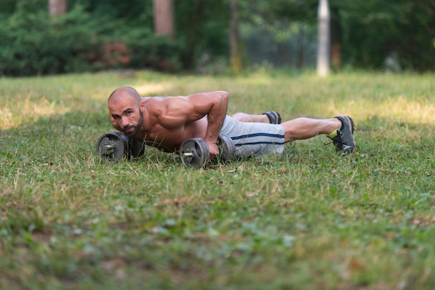 Zdjęcie młody sportowiec mięśni robi pompki z hantlami jako część treningu kulturystycznego treningu na świeżym powietrzu sport i fitness koncepcja zdrowego stylu życia fitness mężczyzna