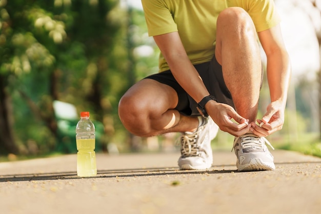 Młody sportowiec wiąże buty do biegania z wodą Energy Drink męski biegacz gotowy do joggingu poza azjatą Fitness spacery i ćwiczenia w parku rano dobre samopoczucie i koncepcje sportowe